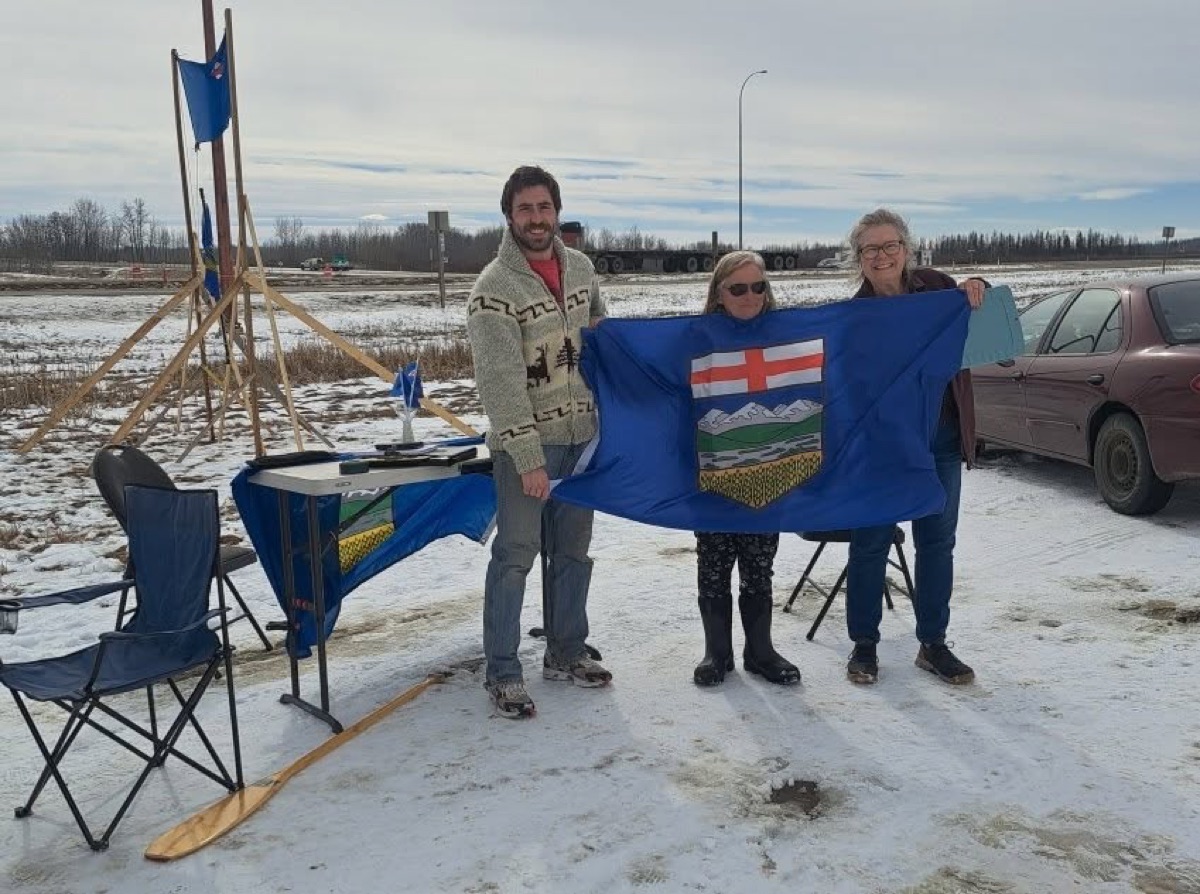 Volunteers holding the Alberta flag at a winter roadside signing table