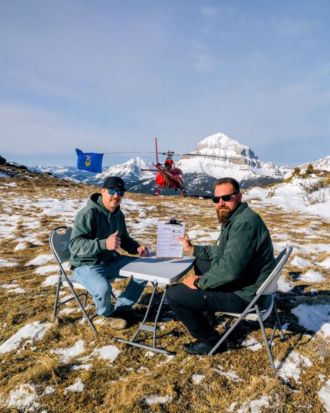 Canvassers signing at a table on a mountaintop with a helicopter behind